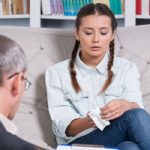 Young woman with tissue in hand sitting on coach talking to doctor - Mental Health Services at North Mississippi Primary Health Care